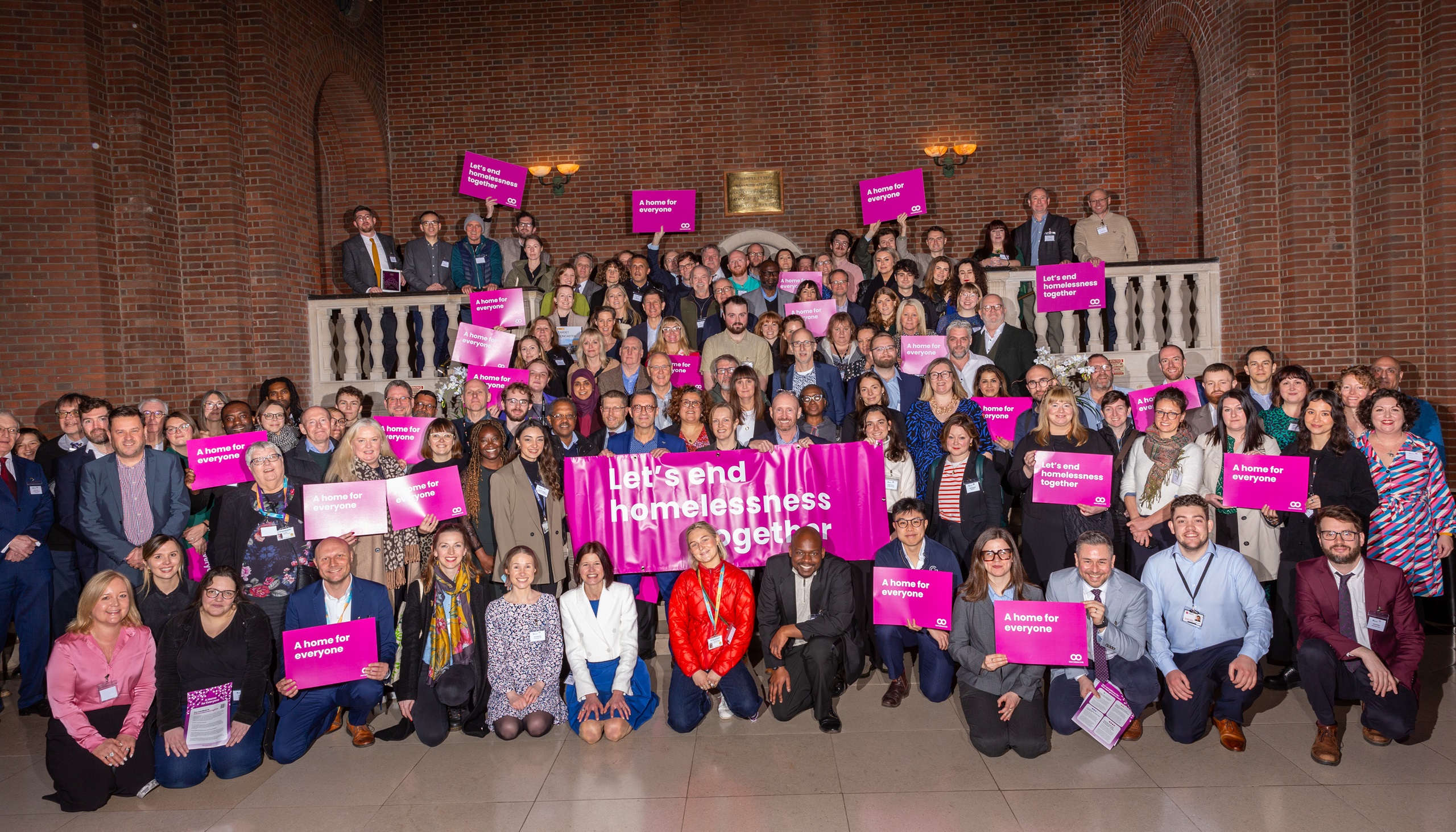 A large group of people representation the organisations attending lobby day, holding signs which say 'A Home for Everyone'